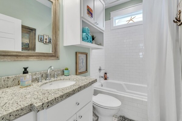 Une salle de bain avec deux lavabos, une baignoire et des toilettes. Un miroir est placé au-dessus des lavabos, et une étagère contient des serviettes et des objets décoratifs.