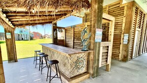 Una zona de bar con barra de madera, techo de paja, una escultura de metal decorativa y un letrero que indica un espacio sin estrés.