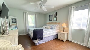 Ein Schlafzimmer mit Bett, Nachttisch, Lampe, Deckenventilator und einem Fenster mit Vorhängen.