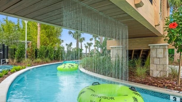 Une piscine avec des bouées gonflables vertes portant l’inscription « Windsor Island Resort » et une cascade décorative.