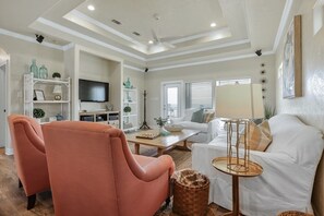 A living room with a white sofa, a peach-colored armchair, a coffee table, and a TV mounted on the wall. - ALL DECKED OUT - 2 Bedroom, 2 Bath, Sleeps 6 - Beach Front! (Crystal Beach)