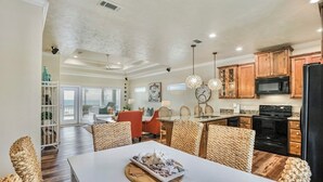 A spacious kitchen with wooden cabinets, a black stove, and a dining area with wicker chairs and a white table. - ALL DECKED OUT - 2 Bedroom, 2 Bath, Sleeps 6 - Beach Front! (Crystal Beach)