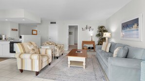 A living room with a sofa, armchairs, a coffee table, a lamp, and a painting on the wall. - Riverside Club 1 Bed Overlooking Marco River (Marco Island)
