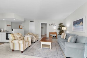 A living room with a sofa, armchairs, a coffee table, a lamp, and a painting on the wall. - Riverside Club 1 Bed Overlooking Marco River (Marco Island)