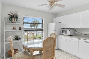 A kitchen with white cabinets, a microwave, and a dining area with a table and chairs. - Riverside Club 1 Bed Overlooking Marco River (Marco Island)