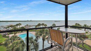 Een balkon met uitzicht op een zwembad en palmbomen, een tafel en stoelen.