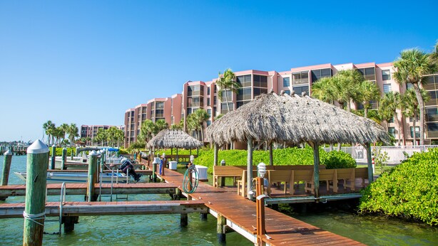 Een hotel aan het water met rieten parasols, houten looppaden en palmbomen.
