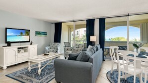 A living room with a sofa, TV, and dining area with chairs and a table. - Marco Retreat I Direct Beach Access Across Street (Marco Island)