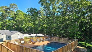 Una terraza de madera con piscina, sillas de descanso y sombrillas.
