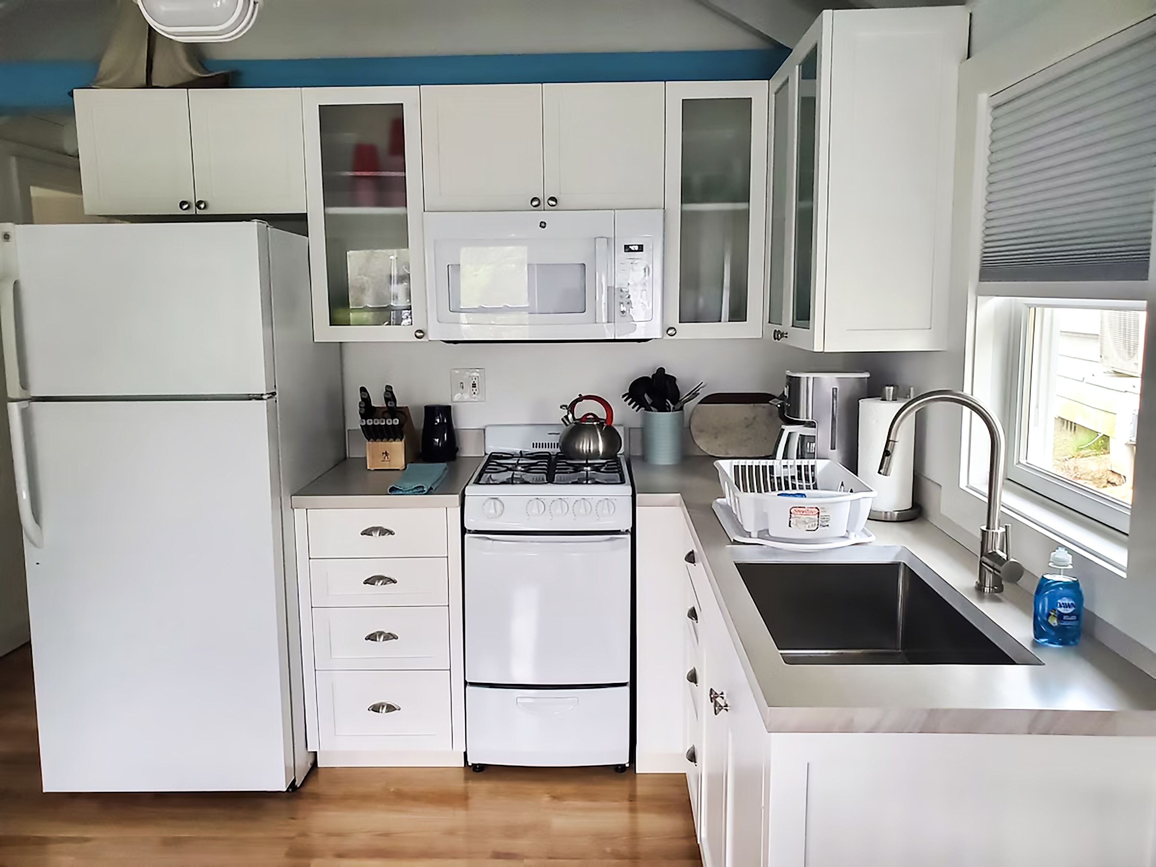 A compact kitchen with white cabinets, a microwave, a gas stove, a sink, and a refrigerator.