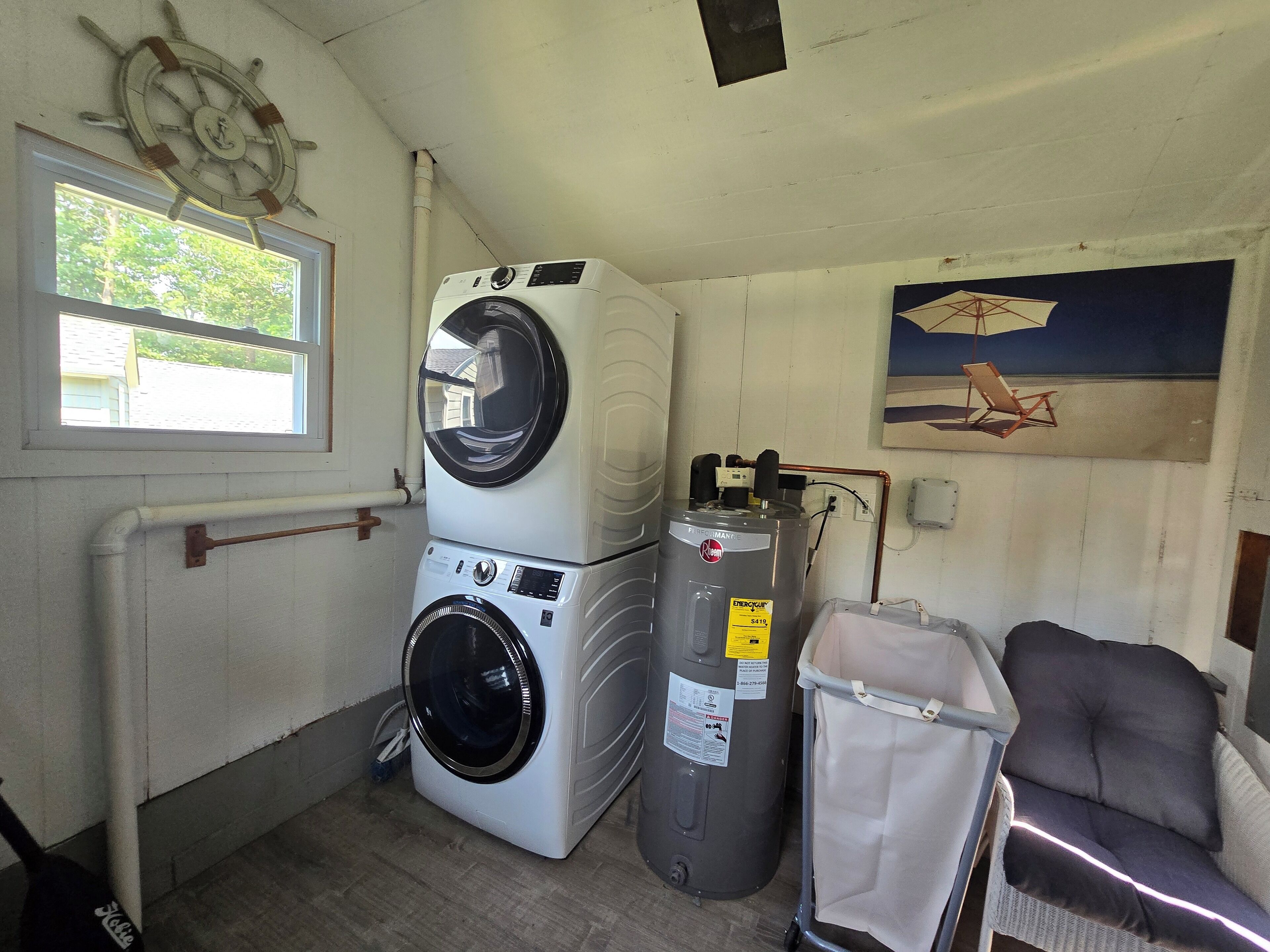 A laundry room with stacked washers and dryers, a water heater, and a chair.