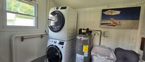 A laundry room with stacked washers and dryers, a water heater, and a chair.