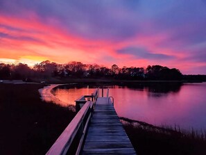 A wooden pier extending into a calm body of water, with a sunset in the background.