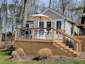 A wooden deck with outdoor furniture and a large umbrella, leading to a house with multiple windows and a covered porch.