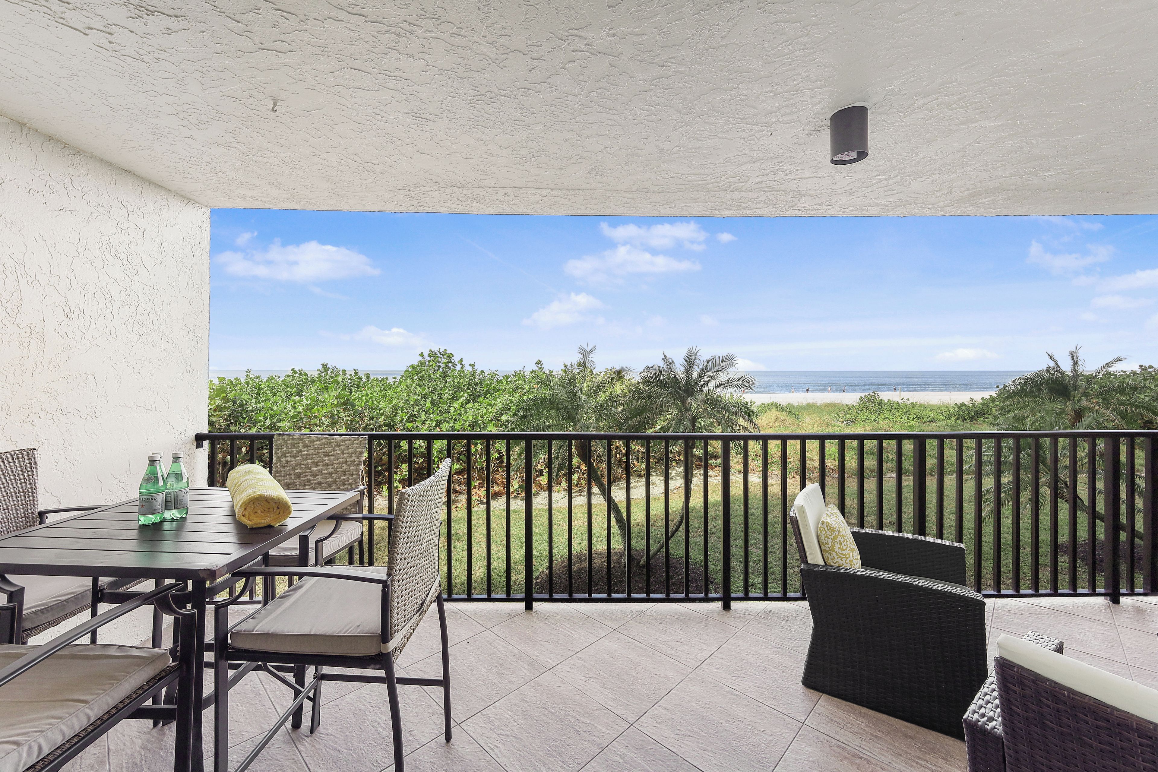 A balcony with a view of the ocean, a table with chairs, and a bottle of water.