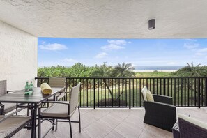 A balcony with a view of the ocean, a table with chairs, and a bottle of water.