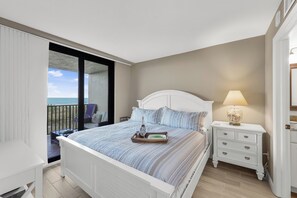 A bedroom with a bed, a bedside table with a lamp, and a view of the sea.