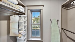 A walk-in closet with shelves for folded clothes, a window with a view, and an ironing board.