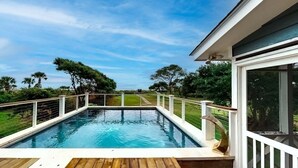 A swimming pool with a wooden deck, surrounded by a white railing and a glass enclosure. - Classic Oceanfront beach home with large screened in porch overlooking ocean! (Isle of Palms)