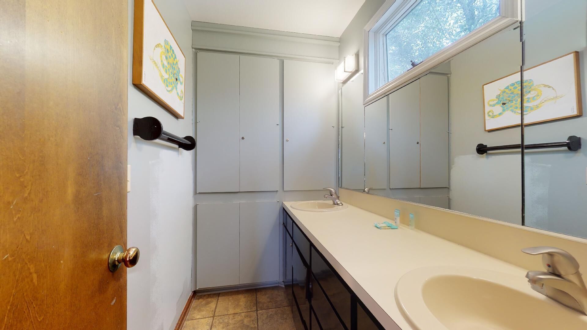 A bathroom with a wooden door, white cabinets, a large mirror, and a sink.