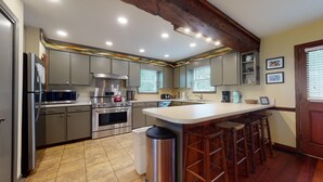 A modern kitchen with stainless steel appliances, a large island with bar stools, and a wooden ceiling. - Classic Oceanfront beach home with large screened in porch overlooking ocean! (Isle of Palms)