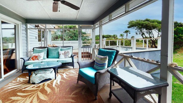 A covered outdoor seating area with wicker furniture and a view of a pool. - Classic Oceanfront beach home with large screened in porch overlooking ocean! (Isle of Palms)