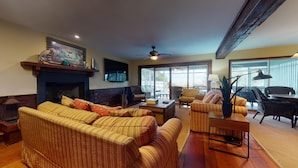 A cozy living room with a fireplace, comfortable seating, and a large window offering a view of the outdoors. - Classic Oceanfront beach home with large screened in porch overlooking ocean! (Isle of Palms)