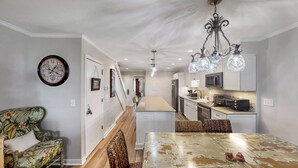 A modern kitchen with a central island, white cabinetry, and a chandelier. - Oceanfront Wild Dunes villa-beach access, community pool & screened porch! (Isle of Palms)