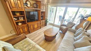 A living room with a television, wooden cabinets, wicker furniture, and a view through a glass door. - Sandy Key 231:  3 BR / 2 BA Gulf Front Condo in Perdido Key, FL  Sleeps 8 (Pensacola)