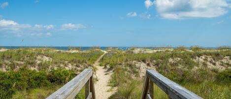 A wooden boardwalk leading to a beach with dunes and sparse vegetation.