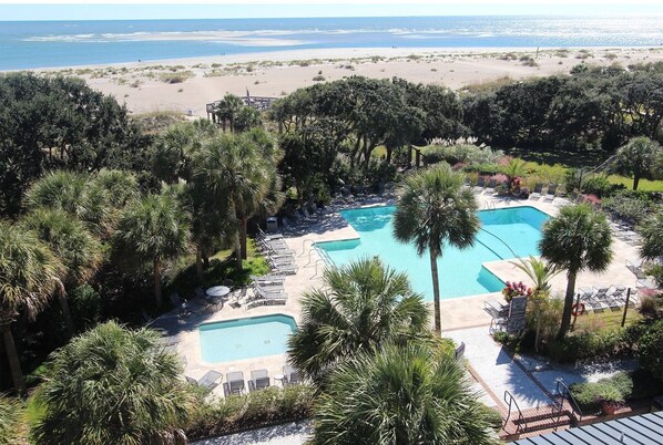 Relax by the pool surrounded by lush greenery and palm trees, with a scenic ocean view.