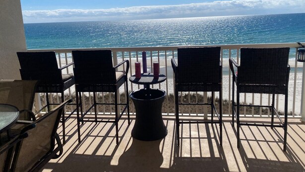 Un balcon avec vue sur l’océan, comprenant quatre chaises en osier, une petite table ronde et une poubelle.