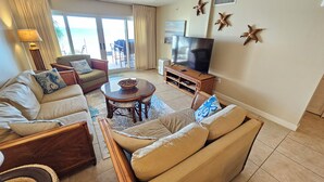 Un salon comprenant un canapé, des fauteuils, une table basse et un téléviseur. Les murs sont décorés de motifs d’étoiles de mer, et les fenêtres offrent une vue sur l’extérieur.