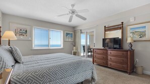 Ein Schlafzimmer mit Bett, Schminktisch, Fernseher, Deckenventilator und großen Fenstern.