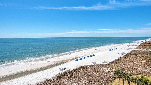 Ein Strand mit weißem Sand, klarem, blauem Wasser und einer Holzpromenade.