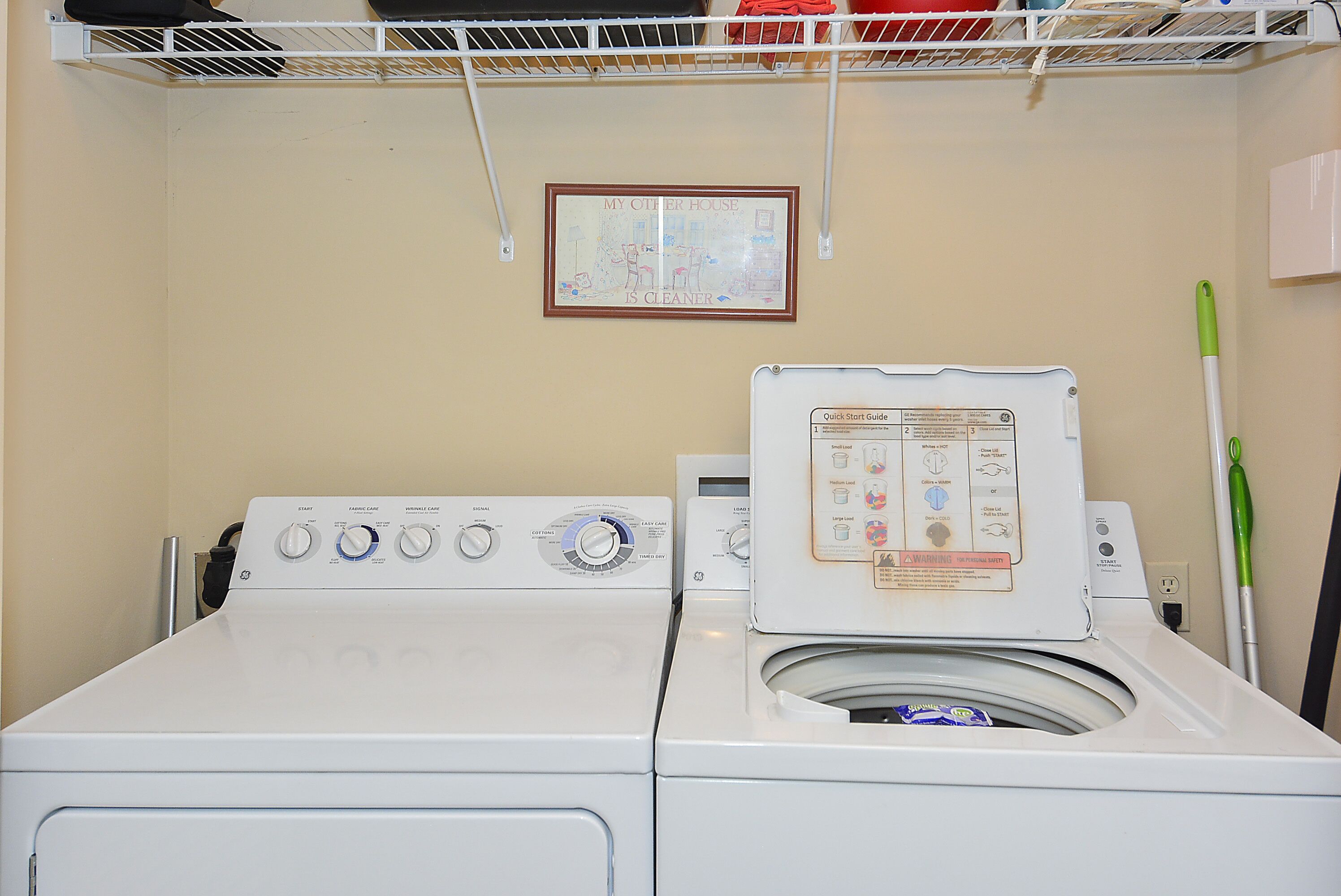 A front-loading washing machine with a control panel, a safety warning label, and a Quick Start Guide.