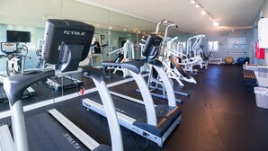 Een sportschool met meerdere loopbanden, trainingsapparaten en een grote spiegelwand.