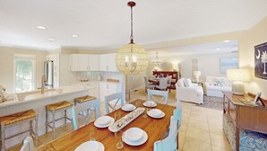 Een moderne keuken met witte kasten, een centraal eiland en een eetgedeelte met een houten tafel voor vier personen.