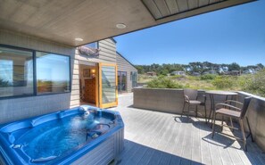 A hot tub on a wooden deck with outdoor furniture and a view of the surrounding landscape.