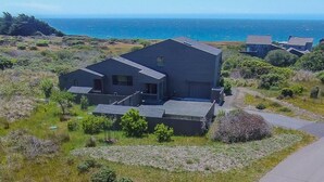 Una casa moderna de dos pisos amb teulat pla, situada en un turó verd amb vistes clares a la costa i a l'oceà.