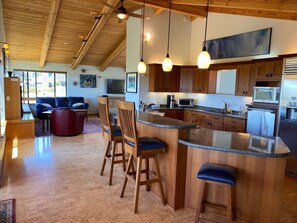 A modern kitchen with a bar area, wooden chairs, and pendant lighting.