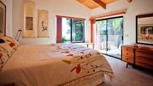 Une chambre avec un grand lit, un plafond en bois, une porte-fenêtre coulissante donnant sur un balcon et une commode.