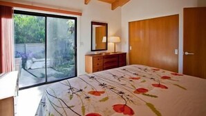 Une chambre à coucher comprenant un lit, une commode, un miroir et une porte-fenêtre coulissante donnant sur un espace extérieur.