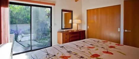 A bedroom with a bed, a dresser, a mirror, and a sliding glass door leading to an outdoor area.