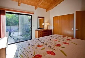A bedroom with a bed, a dresser, a mirror, and a sliding glass door leading to an outdoor area. - Brown-Hansen - Whitewater Sea Ranch Escape (Sea Ranch)