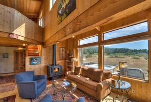 A cozy cabin interior with a fireplace, wooden walls, and large windows offering a view of the outdoors.