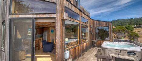 A modern wooden building with large glass windows, a hot tub, and a deck.
