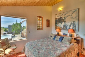 A bedroom with a large bed, a window, a chair, and a painting on the wall.