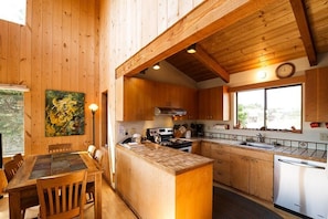 A wooden interior with a dining area, kitchen, and large windows.