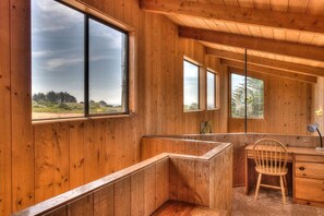 A cabin interior with wooden walls, a desk, a chair, and large windows offering a view of the outdoors. - Clisham - Sea Ranch Cozy 2BR Loft Home (Sea Ranch)